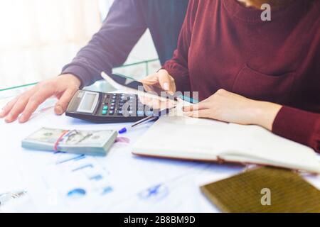 Business woman and man works at home, remote work at home, with laptop and notepad, takes notes on the phone, counts on a calculator. Close up of female accountant or banker making calculations. Savings, finances and economy concept Stock Photo