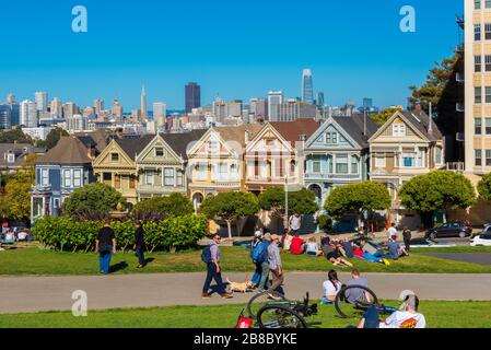 People relaxing in park in front of the Painted Ladies Houses in San Francisco, California, USA. The city skyline can be seen in the background. Stock Photo
