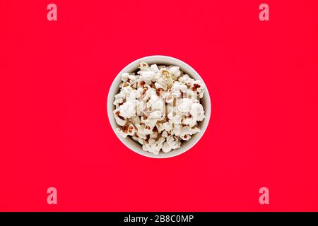 Popcorn in a white bowl on red background. Top view Stock Photo