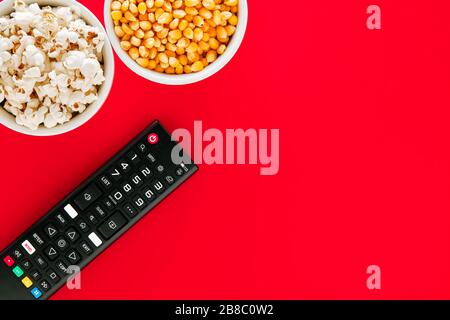 Bowl of popcorn and a bowl of maize grain with TV remote control on a red background. Watch TV or movies in leisure time.. Stock Photo