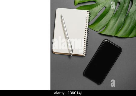 Workspace with pen, tropical monstera leaves, notebook, smartphone with copy space on grey and white background minimal style. Creative flat lay of of Stock Photo