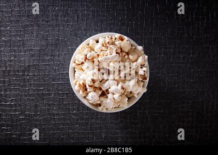 Popcorn in a white bowl on black textured background. Top view Stock Photo
