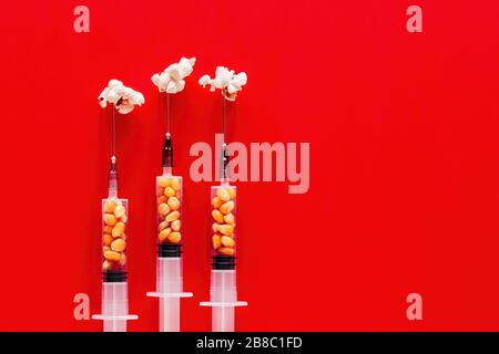 Popcorn grains in the syringe on red background. Genetic modification or making popcorn concept. Stock Photo