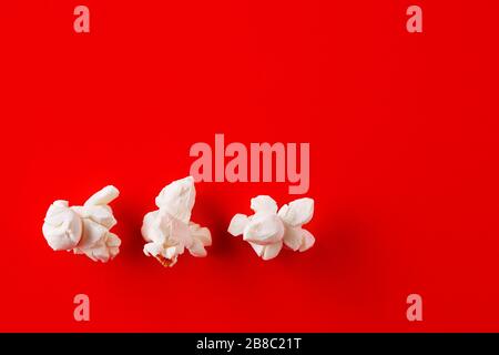 Three popcorns in a row on red background. Close up macro top view. Stock Photo