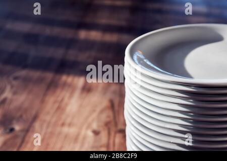 Pile of white plates on the wooden table of a restaurant or cafe under natural afternoon sunlight. Stock Photo