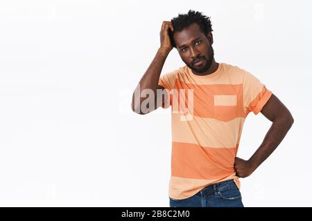Troubled and unsure pretty african-american bearded guy have no idea how thing works, scratching head and looking questioned or confused, trying Stock Photo