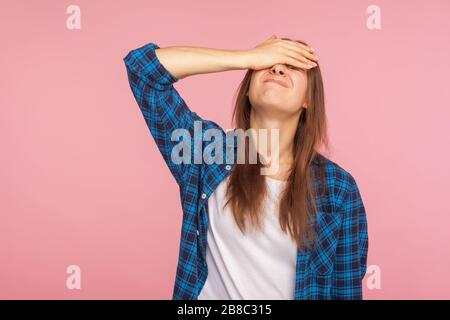 Portrait of unlucky girl in checkered shirt standing with facepalm gesture, feeling regret and sorrow, blaming herself for mistake, frustrated by defe Stock Photo