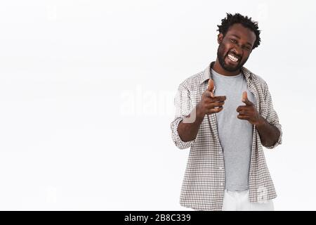 Cheeky and flirty handsome carefree african-american bearded male, wear casual outfit, pointing finger pistols camera as cheering, encourage someone Stock Photo