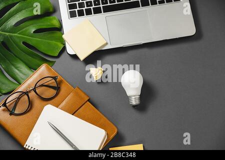 Concept brainstorming and new idea. Creative top view flat lay of desk with light bulb, laptop, pen, monstera leaves, eyeglasses and notebook with cop Stock Photo