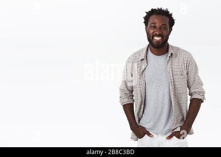 Outgoing, sociable happy african-american male with beard, afro haircut, hold hands in pockets and smiling broadly, looking carefree and enthusiastic Stock Photo