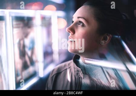Serious thoughtful woman looking at city lights at night in dark. Dramatic face with reflection of billboard signs. Pensive lady thinking. Side view. Stock Photo