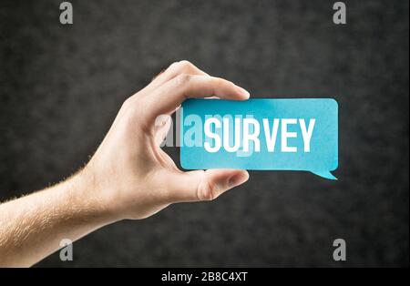 Survey. Giving feedback, market research, questionnaire, user experience and review concept. Hand holding cardboard paper speech bubble. Stock Photo