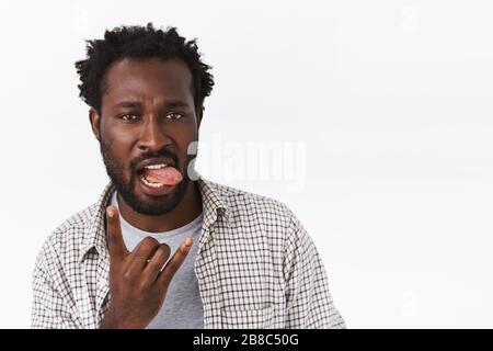 Sassy and cool handsome african-american bearded confident guy, acting all cheeky and coquettish, showing tongue, making rock-n-roll heavy metal sign Stock Photo