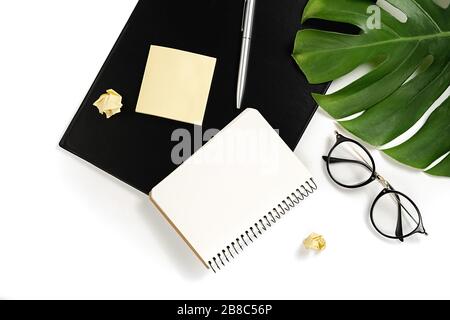 Flat lay, top view office table desk. Workspace with clipboard mockup, pen, green monstera leaves, eyeglasses and notebook on white background minimal Stock Photo