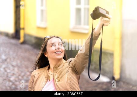 Happy woman taking selfie or vlogger filming video blog. Smiling and laughing person making vlog with digital camera in city. Tourist taking photo. Stock Photo