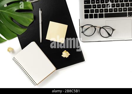 Modern workspace with laptop, pen, monstera leaves, eyeglasses, clipboard, smartphone and notebook with copy space on white background minimal style. Stock Photo