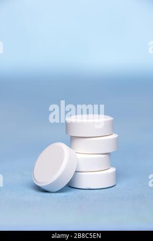 Close-up of large white round tablets of Vitamin C grouped in vertical pile on blue textured surface. One tablet is at the bottom of the pile. Selecti Stock Photo