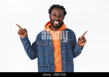 Cheerful handsome african-american guy wear denim autumn jacket, orange hoodie, pointing sideways left and right, smiling and laughing as have two Stock Photo