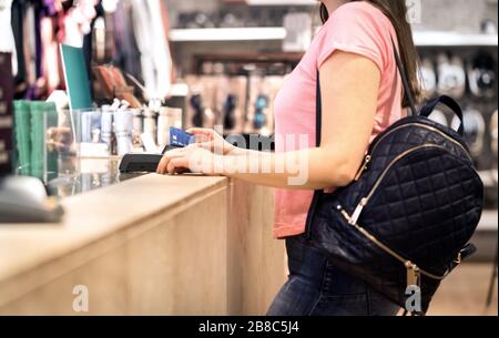 Woman at checkout in fashion store paying with credit card. Customer using payment terminal machine. Standing at counter. Buying and shopping. Stock Photo