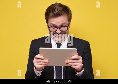 Amazed happy guy in glasses holding using digital tablet looking shocked about social media news, having video chat. Studio shot Stock Photo