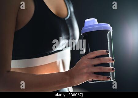 Protein shake after workout and gym training. Fit woman holding bottle of sport drink, whey or healthy smoothie. Fitness athlete with shaker. Stock Photo