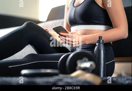 Online workout course, personal trainer service or fitness app in phone. Fit woman using smartphone while working out at home. Stock Photo