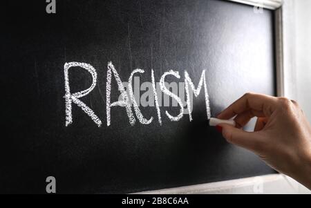 Hand writing the word racism on blackboard. Stop hate. Against prejudice and violence. Lecture about discrimination or stereotypes in school. Stock Photo