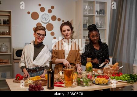 Group of friends smiling at camera while standing in the kitchen and cooking together Stock Photo