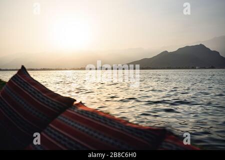 Dhow boat cruise in Musandam Peninsula in Oman at sunset. View from tourist sail ship to mountains and traditional Omani town with mosques. Stock Photo