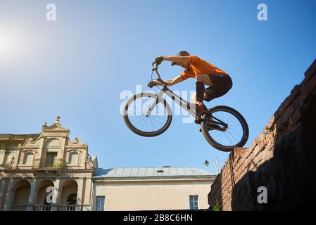 View from below sporty man on a black sport bike in motion performing a somersault. Bike with athlete standing on red bricks. Concept of rest. Stock Photo