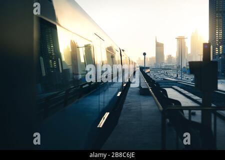 Subway and metro train in city. Futuristic modern public transport. Dubai railway system at sunset with skyscraper buildings and car traffic. Stock Photo