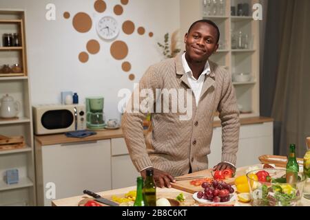 Portrait of African young man looking at camera while cooking in domestic kitchen Stock Photo