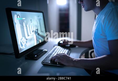 Young man playing video game late at night at home. Gamer streaming fps videogame online. First person shooter. Esports and competitive gaming. Stock Photo