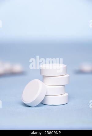 Vitamin C tablets are grouped in vertical pile on blue surface. One tablet is at the bottom of  pile. Two unfocused blister packs at background. Selec Stock Photo