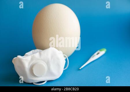 Large white easter ostrich egg in a respirator and a thermometer. Egg, respirator and thermometer. Easter and Coronavirus, Covid-19. Ostrich egg Stock Photo