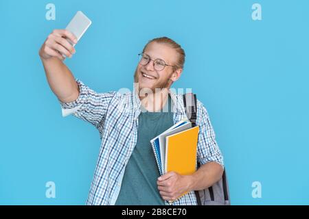 Smiling man student blogger hold phone record vlog isolated on blue background. Stock Photo