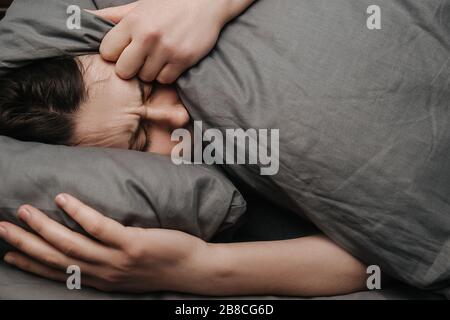 Sad depressed young woman lying on bed covering head with pillow feels unhappy and lonely, cheated unhappy girl suffers hurt from break up Stock Photo