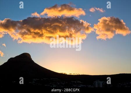 Sunrise over Lion's Head and Signal Hill in Cape Town. As sun inches up over the horizon, the light turns the clouds above a glowing gold. Stock Photo