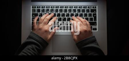 Overhead hacker in the hood working with laptop typing text in the darkroom.  Stock Photo