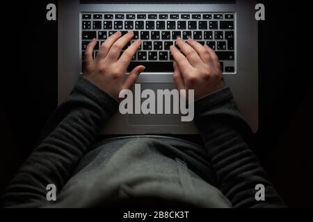 Overhead hacker in the hood working with laptop typing text in the darkroom.  Stock Photo