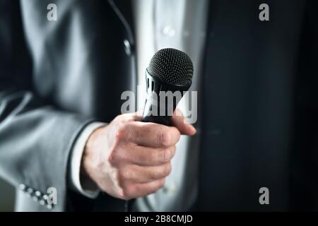 Business man holding microphone. Public speaking and giving speech in suit for audience concept. Fiance, host or best man giving toast with mic. Stock Photo