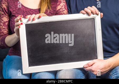 2 people holding empty chalkboard with wooden frame. Friends or a couple showing blank blackboard with copy space for background. Stock Photo