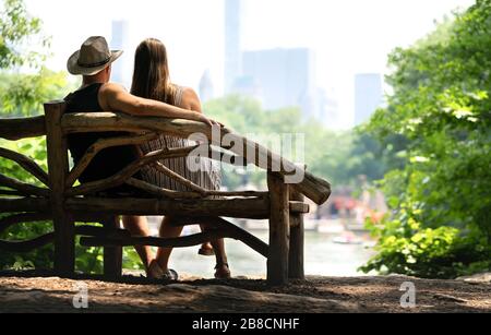 Couple sitting on a park bench and having a romantic first date. Lovers with romance and trust. Back view of happy man and woman watching the building. Stock Photo