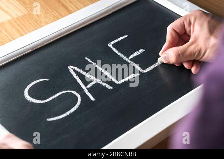 Sale blackboard banner in store, shop or marketplace to promote bargain prices or clearance. Small business owner, salesman or assistant writing text. Stock Photo
