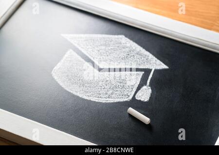 Graduation hat drawn on blackboard with chalk. Applying to college or university concept. Traditional education. Studying or teaching in classroom. Stock Photo