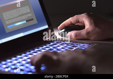 Man installing software in laptop in dark at night. Hacker loading illegal program or guy downloading files. Cyber security, piracy or virus concept. Stock Photo