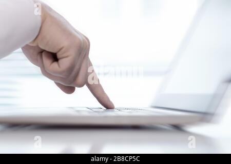 One single finger pressing keyboard button in laptop with blurry background. Man pointing keys with hand, typing or tapping computer. Stock Photo