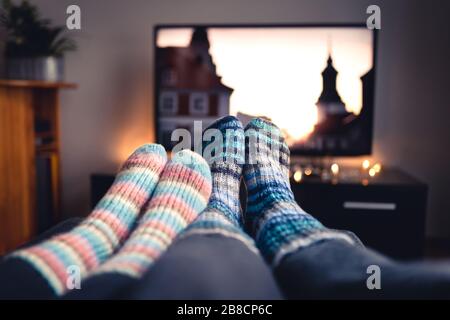Couple with socks and woolen stockings watching movies or series on tv in winter. Woman and man sitting or lying together on sofa couch at home.
