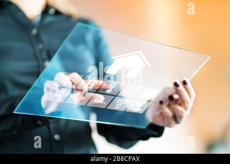 Woman using smart home control application with futuristic transparent glass tablet. Finger touching button to control property. Stock Photo