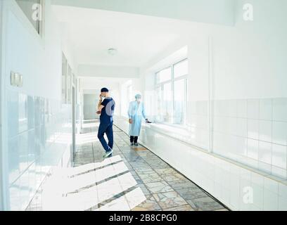 Two men in face masks and lab coats standing at the corridor of the hospital Stock Photo